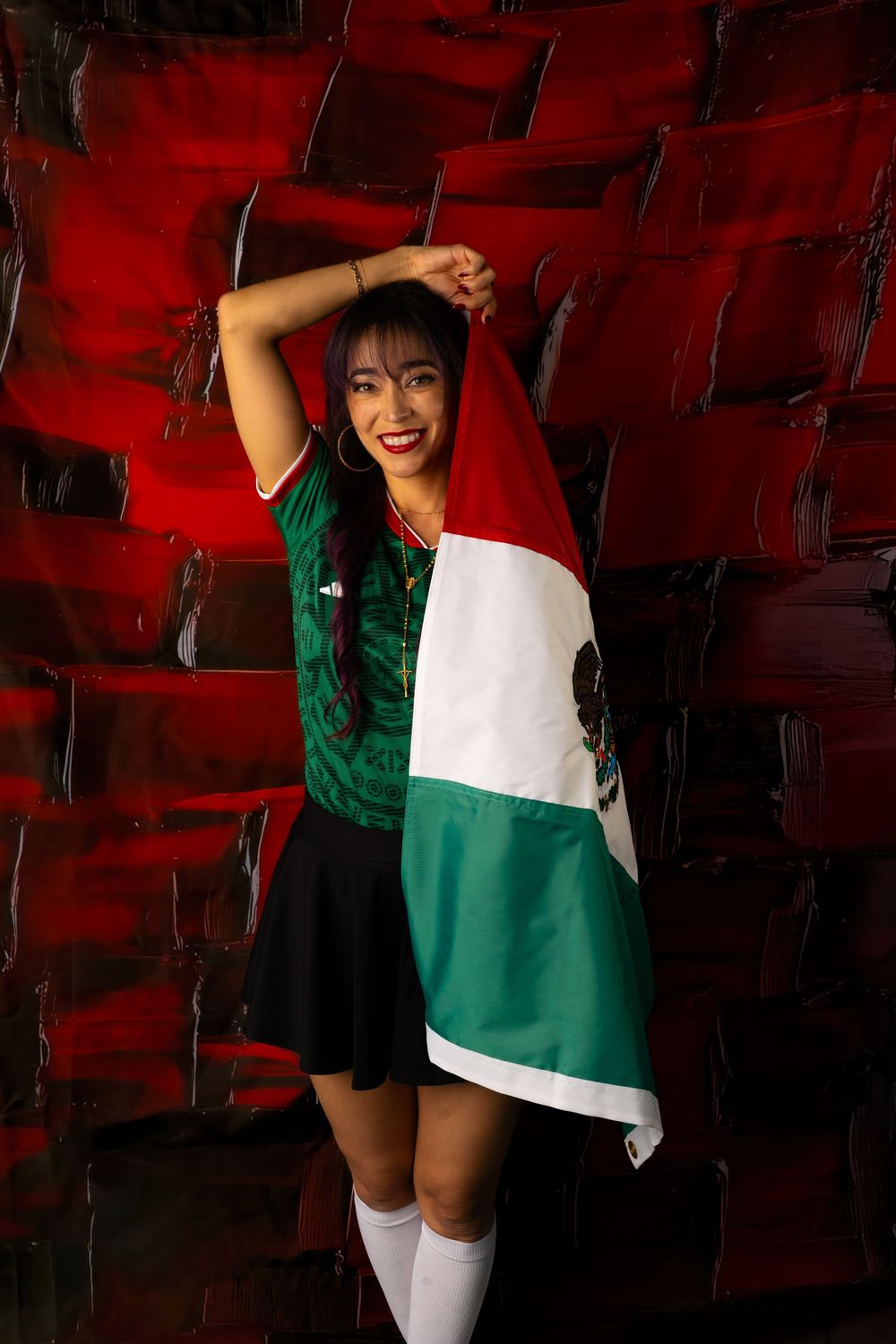 Woman in Mexico soccer jersey holds Mexican flag in stadium with red seats.
