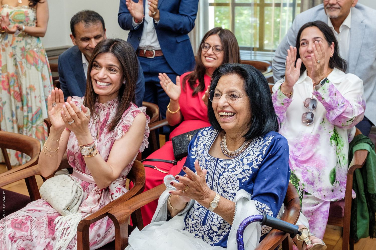 Joyful women in colorful traditional attire clapping and smiling at a festive South Asian celebration.