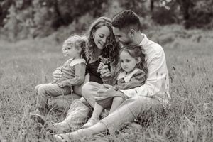 Black and white family photo of parents and two young children sitting together in a grassy field.