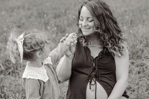 Black and white photo of a smiling pregnant woman with curly hair interacting with a young girl in a field.