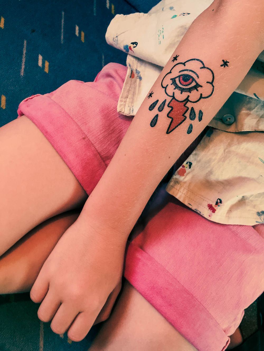 Colorful traditional tattoo of a cloud with an eye and lightning bolt on a forearm.