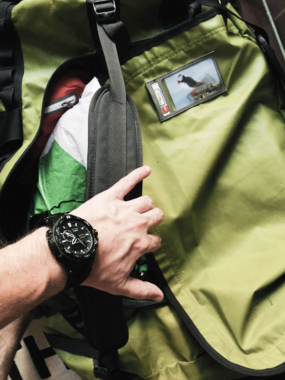 Person wearing a black watch opening a green hiking backpack with gear inside.