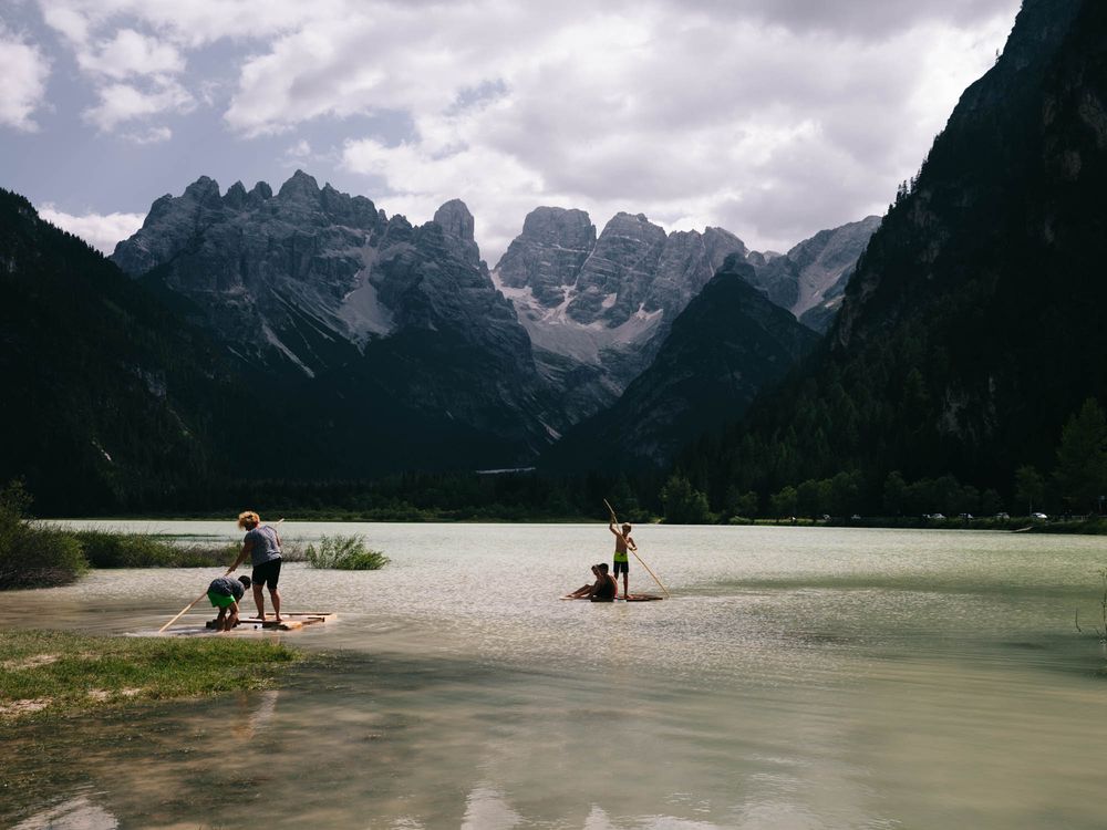 Two people paddleboarding on a serene alpine lake surrounded by dramatic Dolomite mountain peaks in Italy.