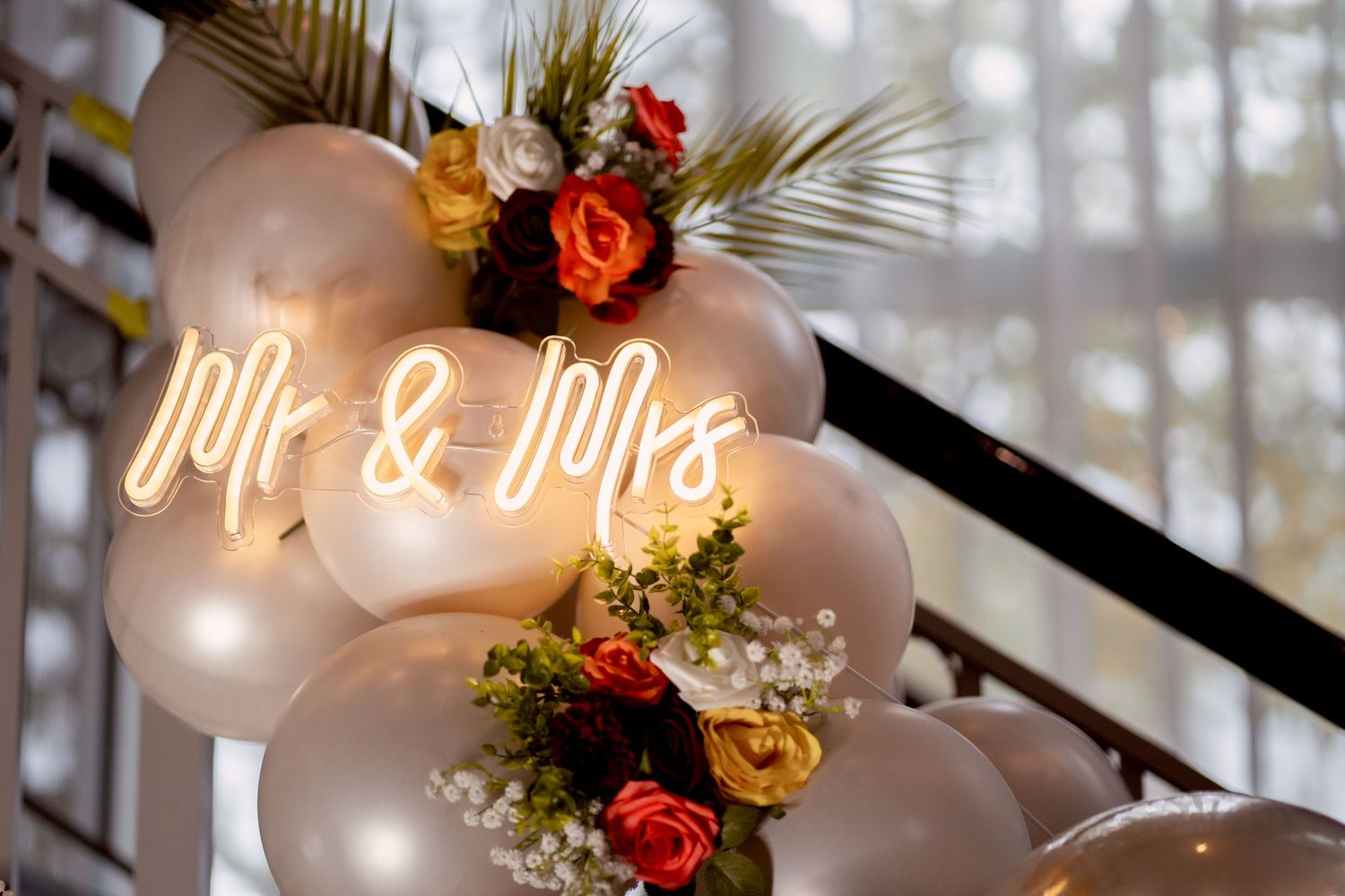 Mr & Mrs neon sign surrounded by white balloons and colorful roses for a wedding decoration.