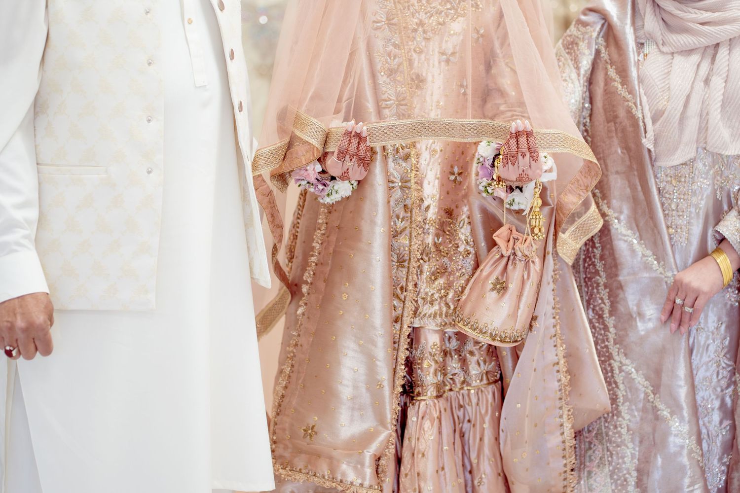 Close-up of elegant blush pink embroidered wedding attire with floral wrist corsages at a South Asian ceremony.