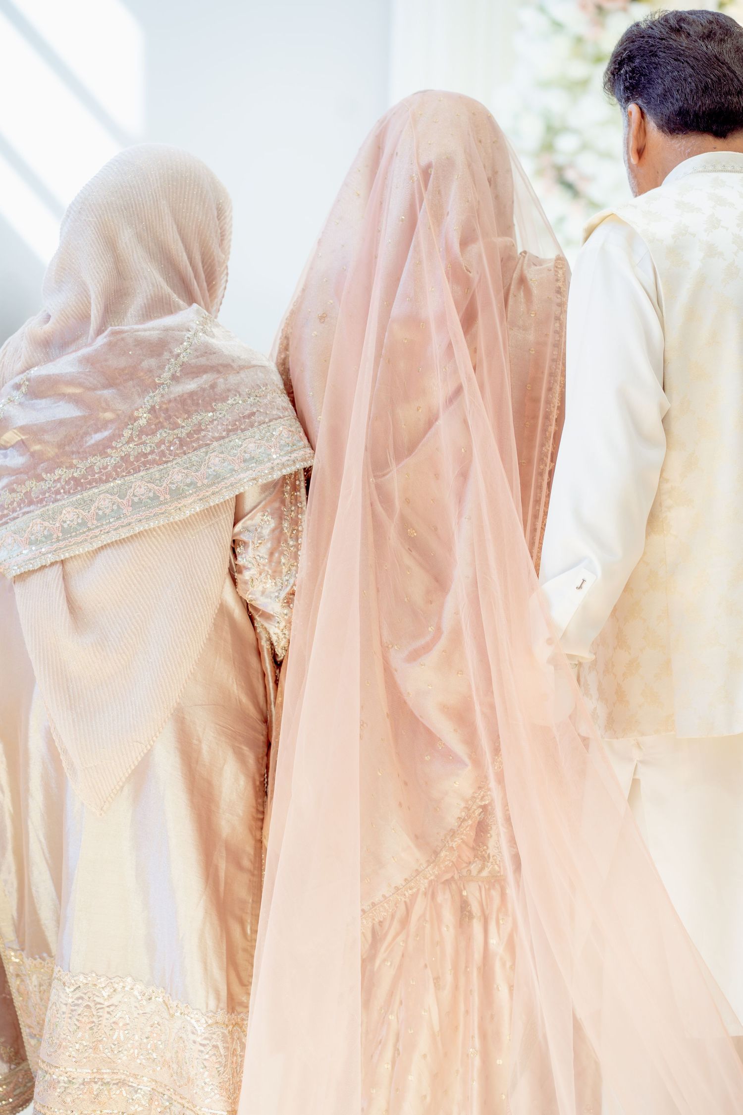 South Asian bride in pink veil with family members in traditional attire at a wedding ceremony.