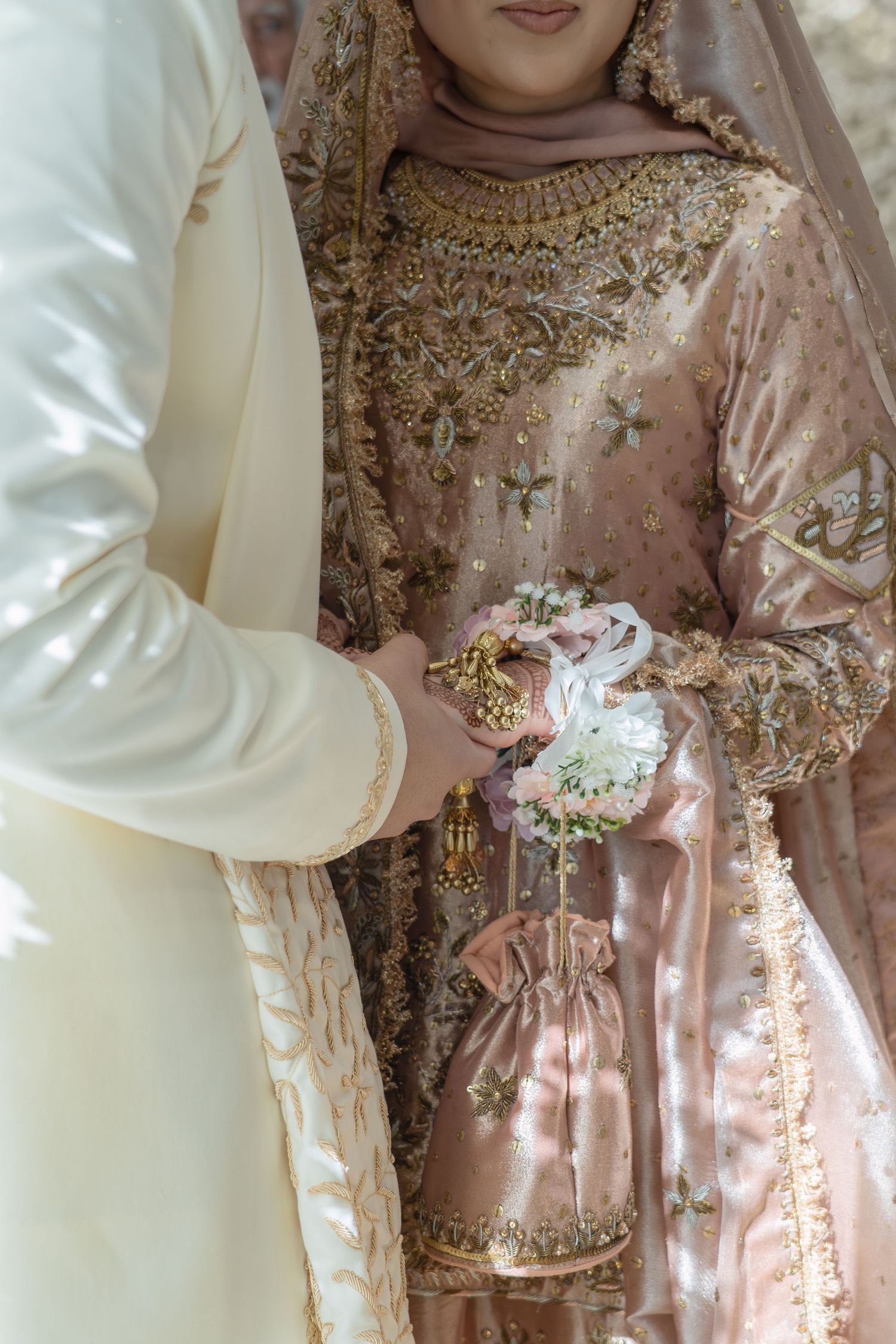 Muslim bride in embroidered pink bridal gown holding floral bouquet with groom in white sherwani at wedding ceremony.