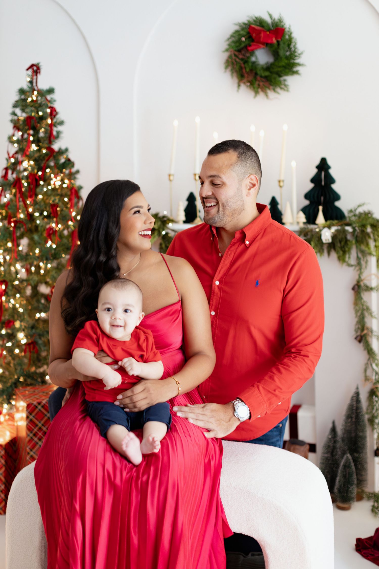 Family in red outfits posing with baby in front of Christmas tree and holiday decorations.