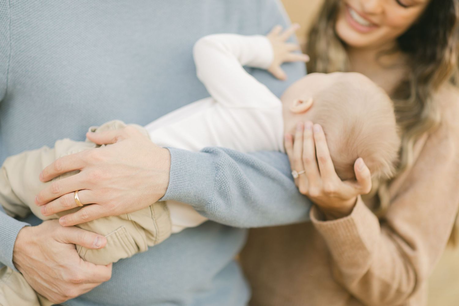 Parents tenderly holding their newborn baby, with mother smiling warmly in a soft, neutral-toned family portrait.