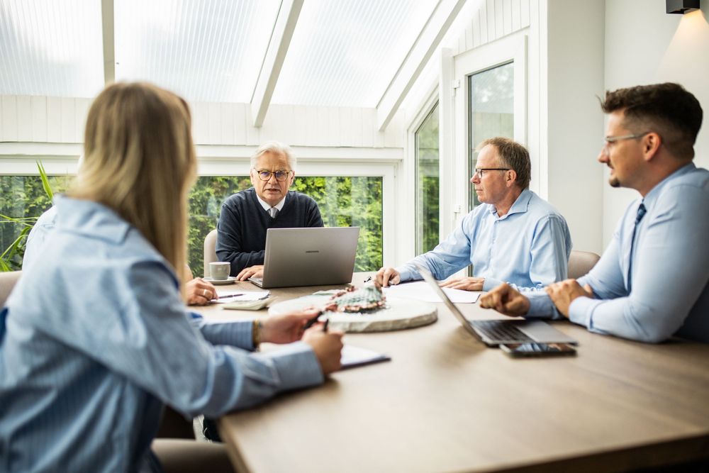 Four business professionals having a meeting around a wooden table in a bright conservatory office.