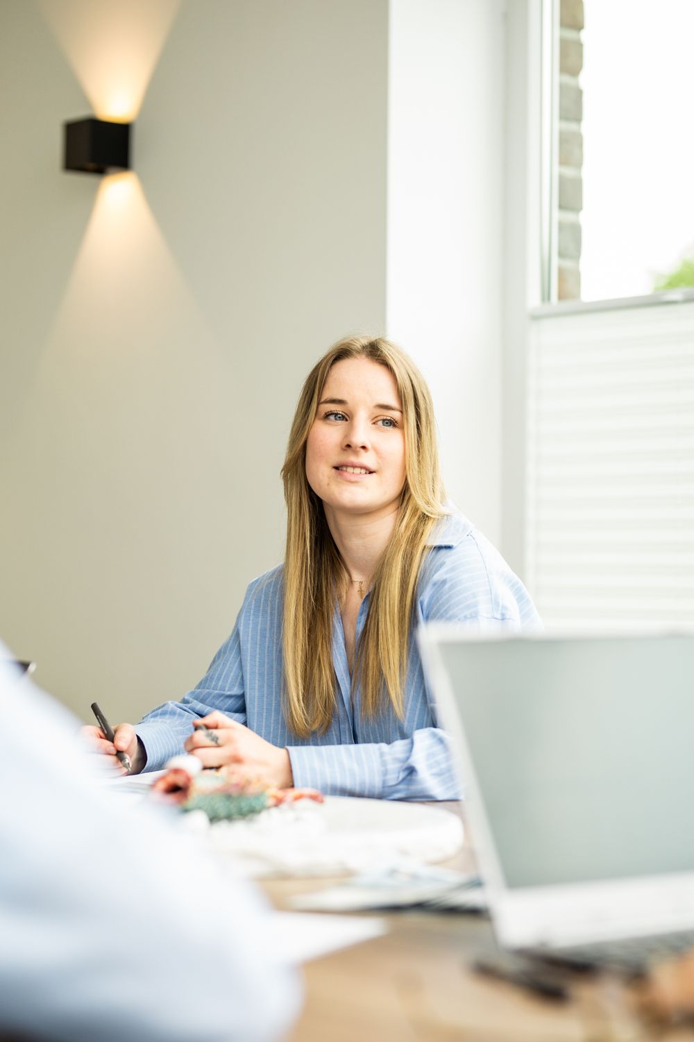 Young blonde businesswoman in blue shirt attentively listening during a professional office meeting.
