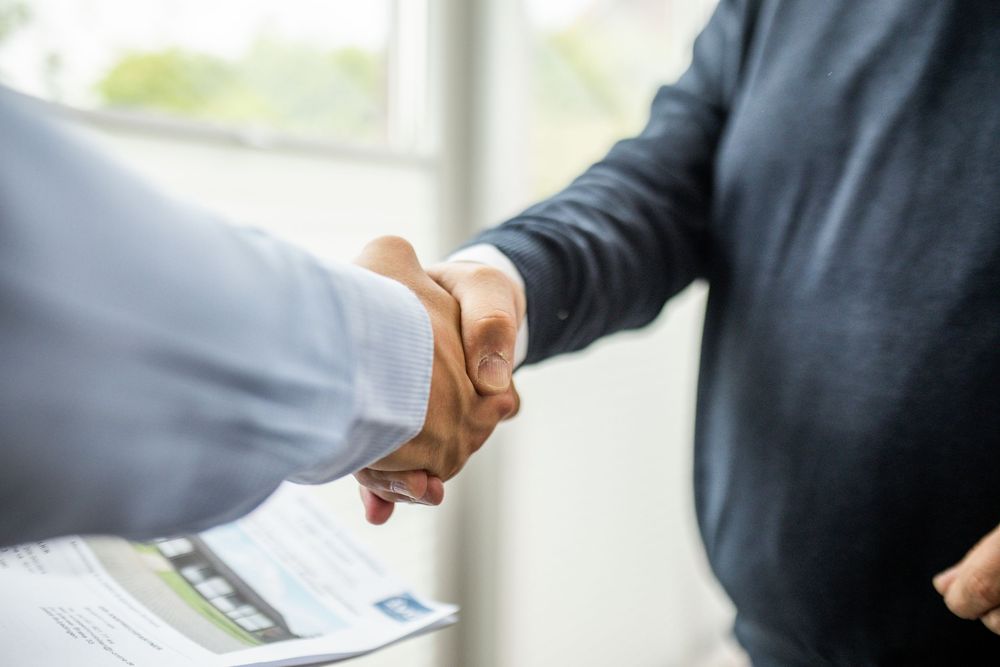 Two business professionals shaking hands over a signed contract, symbolizing a successful business deal or partnership agreement.