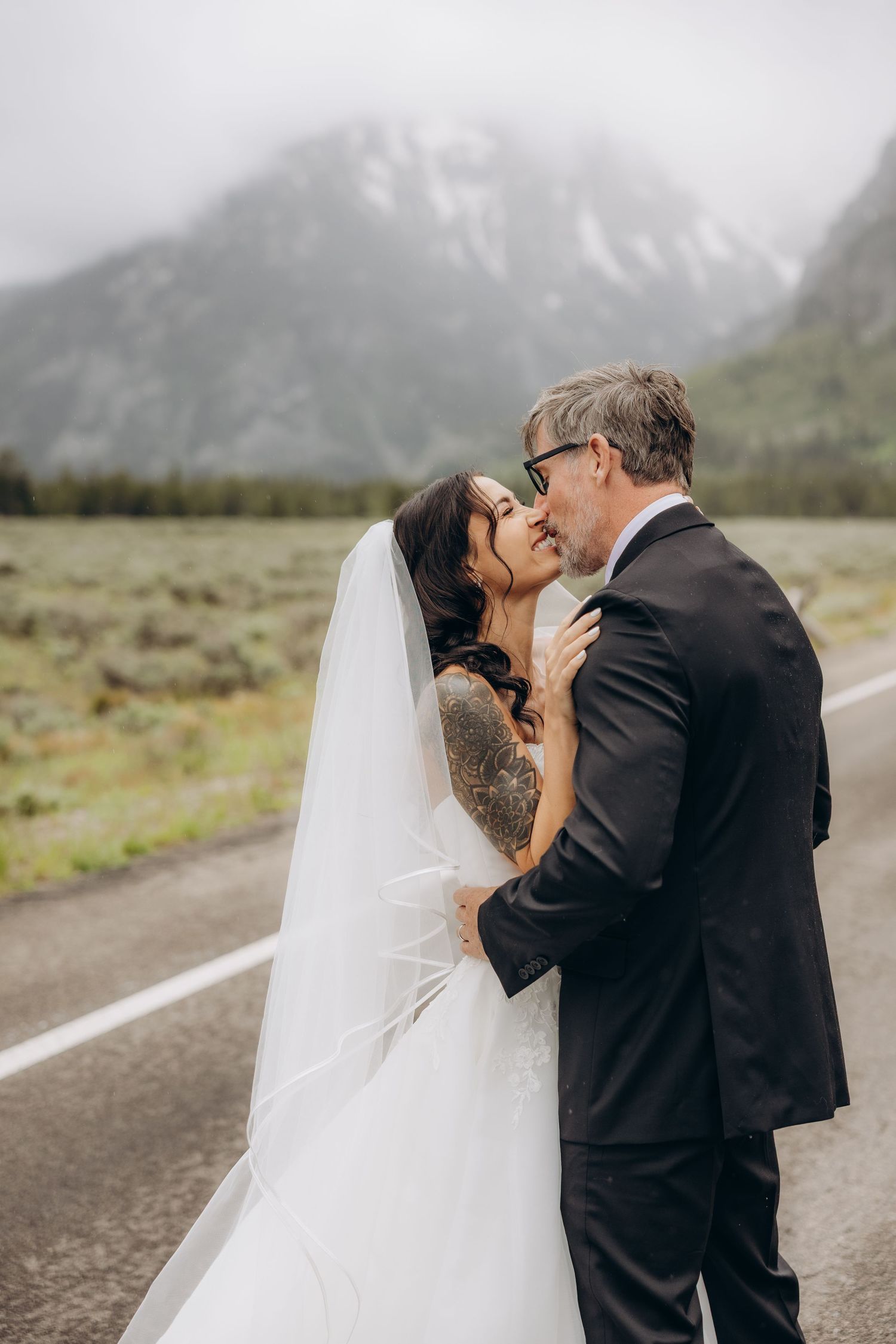 Bride and groom share a romantic moment on a road with misty mountain backdrop at Grand Teton wedding.