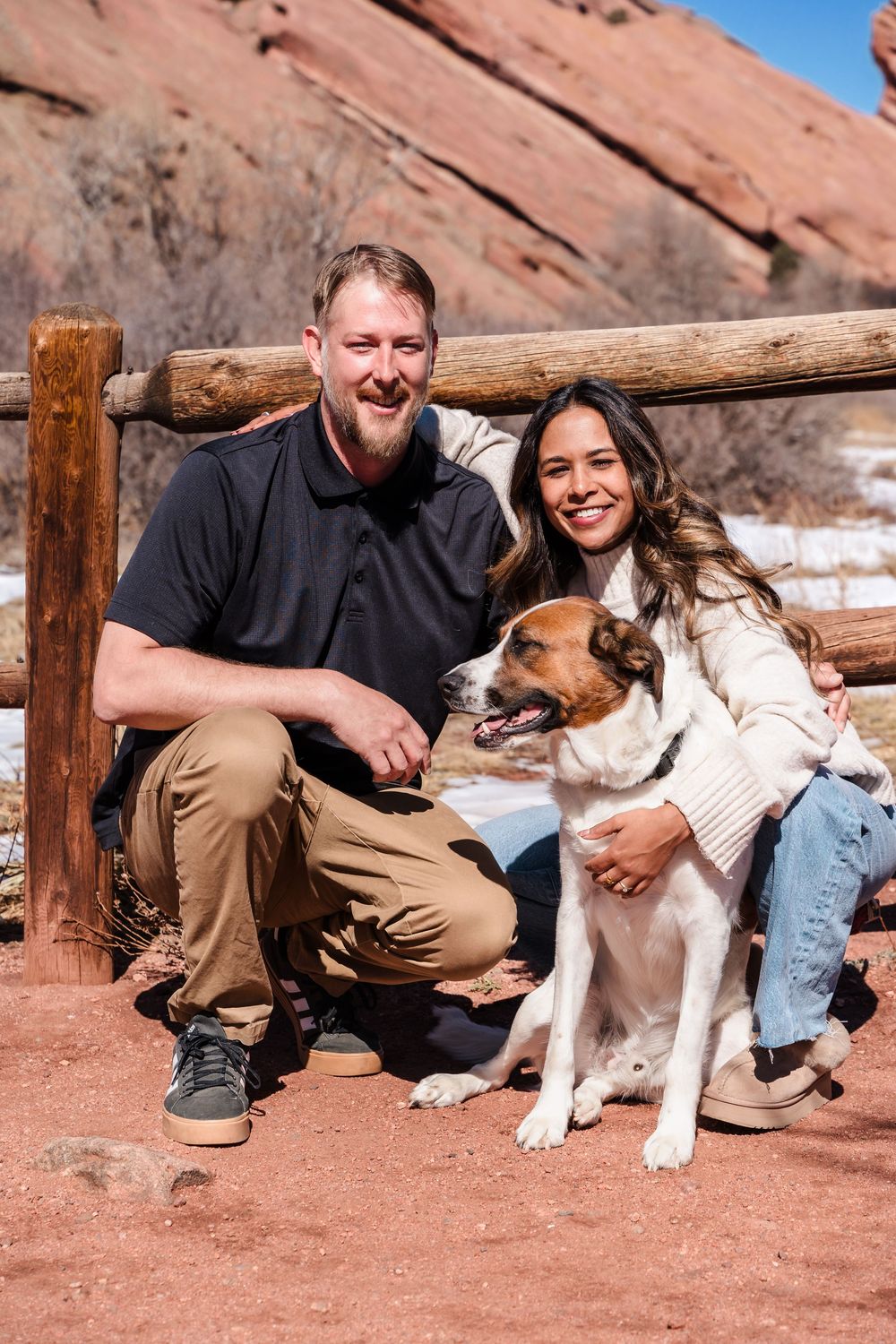 Couple smiling with their dog at Red Rocks Park, Colorado, surrounded by red rock formations.