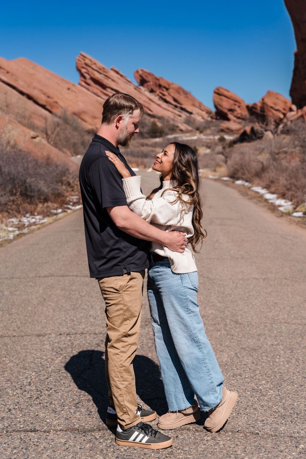 Couple embracing on a road at Red Rocks Amphitheatre, Colorado, surrounded by red rock formations.