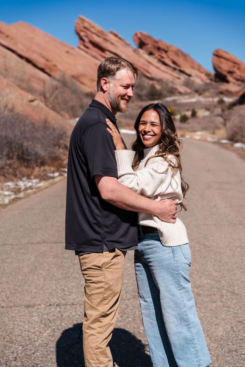Happy couple embracing on a road at Red Rocks Amphitheatre, Colorado, on a sunny day.