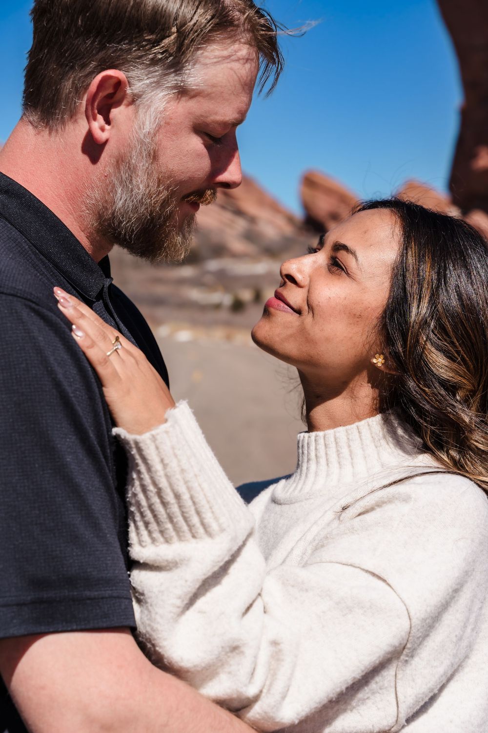 Couple sharing a romantic moment outdoors near red rocks under a clear blue sky.