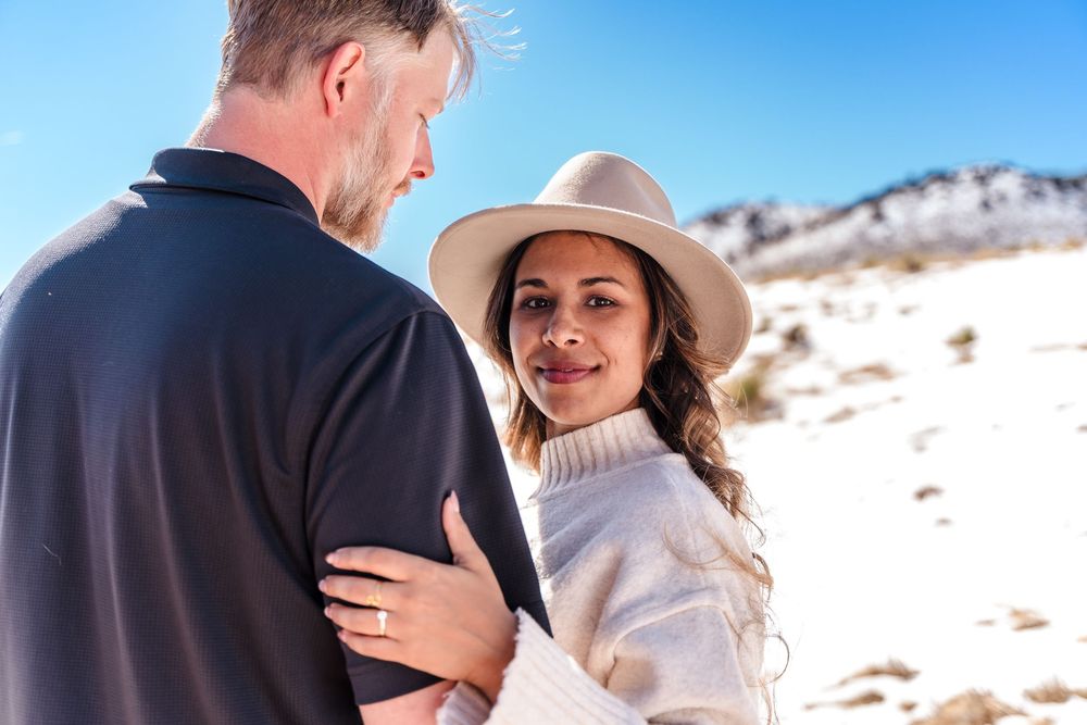 Woman in white sweater and hat embracing a man outdoors in a snowy landscape.