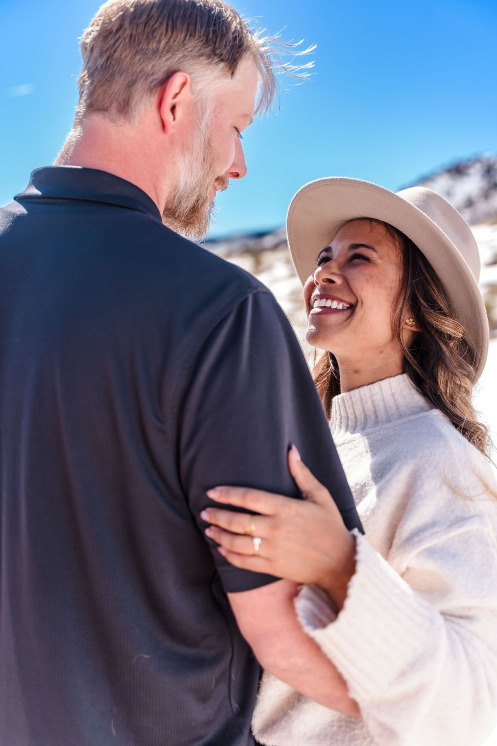 Woman in a cream sweater and hat laughing with her partner at a snowy Colorado outdoor location.