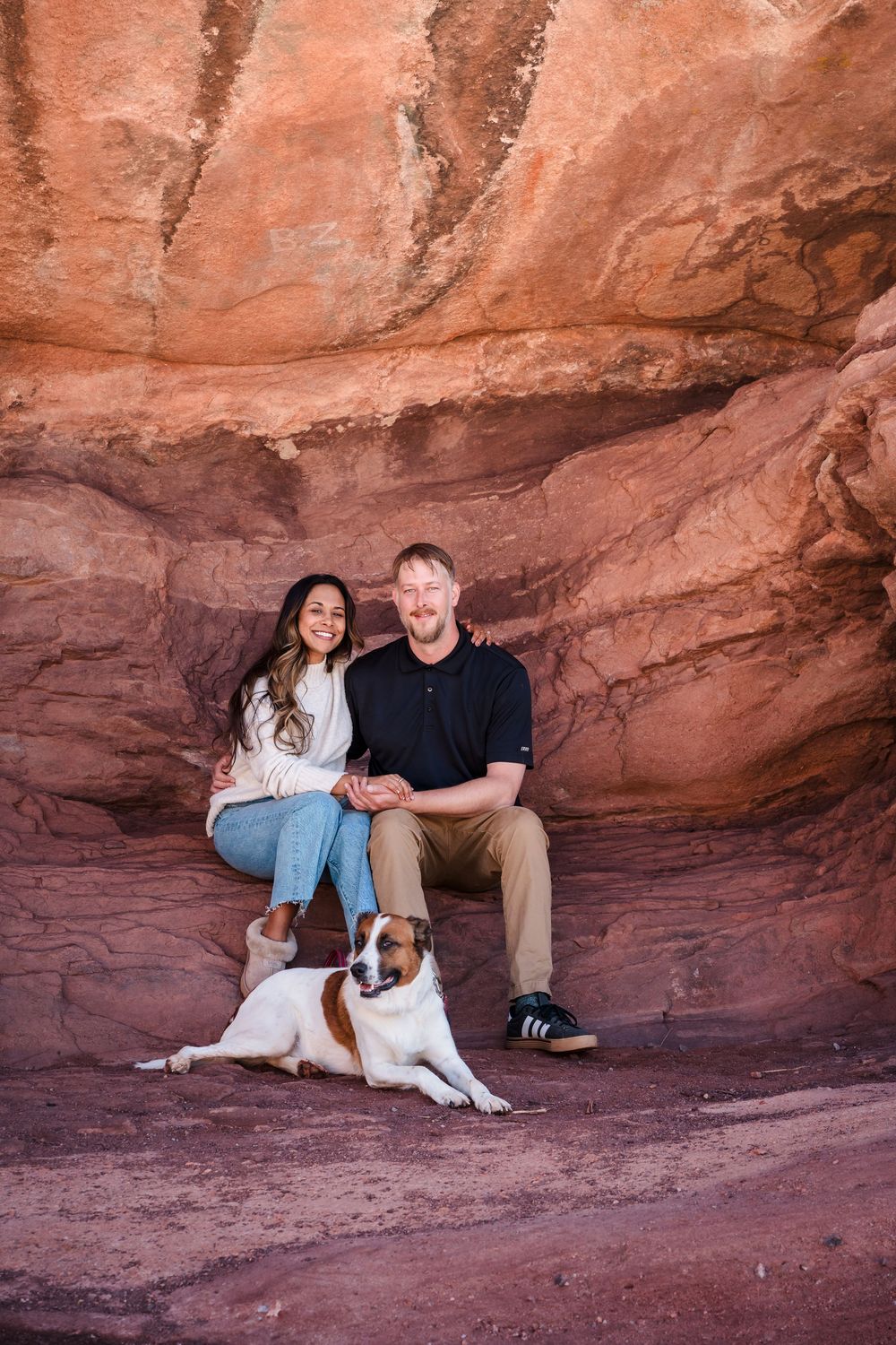 Couple sitting together with their Jack Russell terrier dog against red rock canyon walls outdoors.