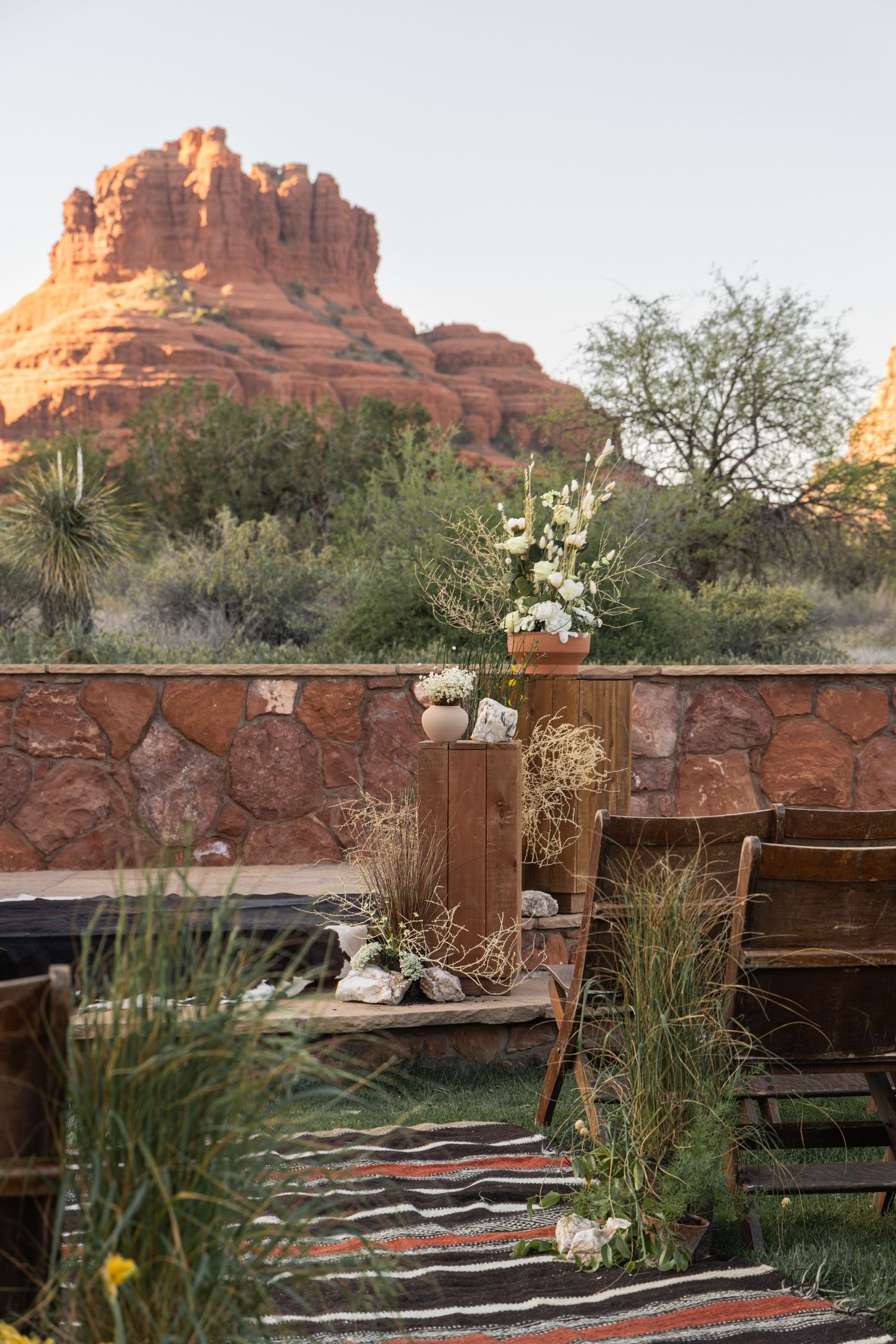 White floral arrangement on wooden pedestal on mountain deck with pine forest backdrop.