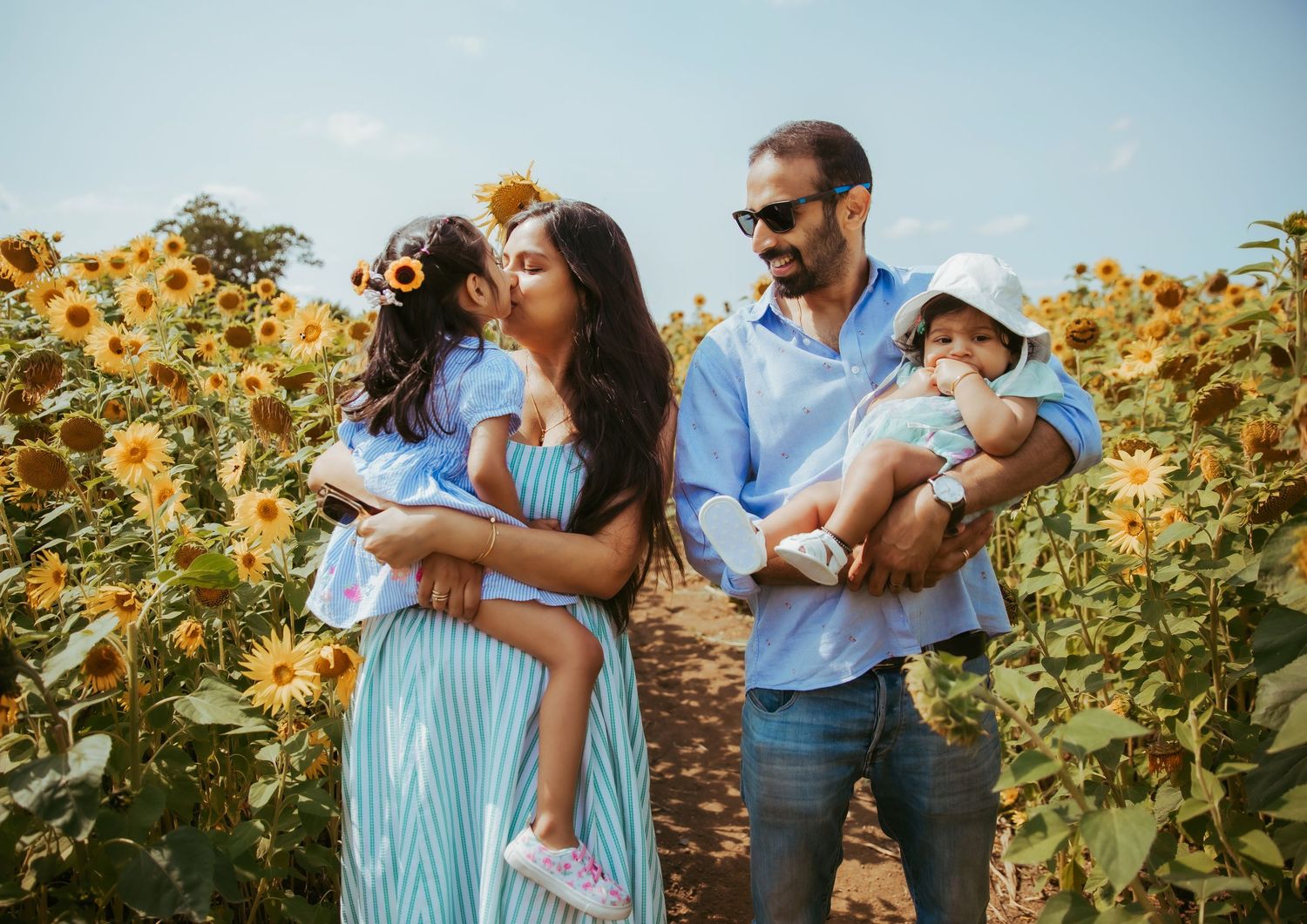 Family posing in sunflower field, mother kissing daughter, father holding baby, sunny day outdoor portrait session Kent