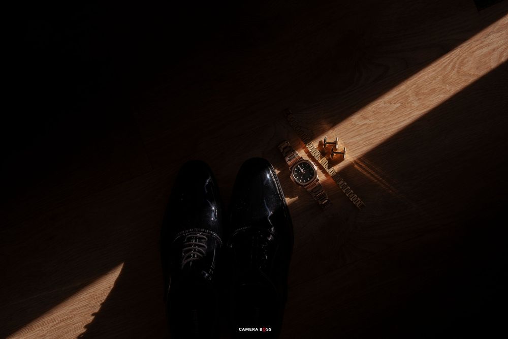 A dramatic shaft of sunlight illuminates polished dress shoes and a watch on a wooden floor.