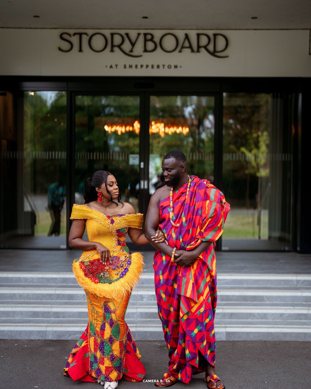 Couple in vibrant African Kente attire posing outside Storyboard at Shepperton venue.