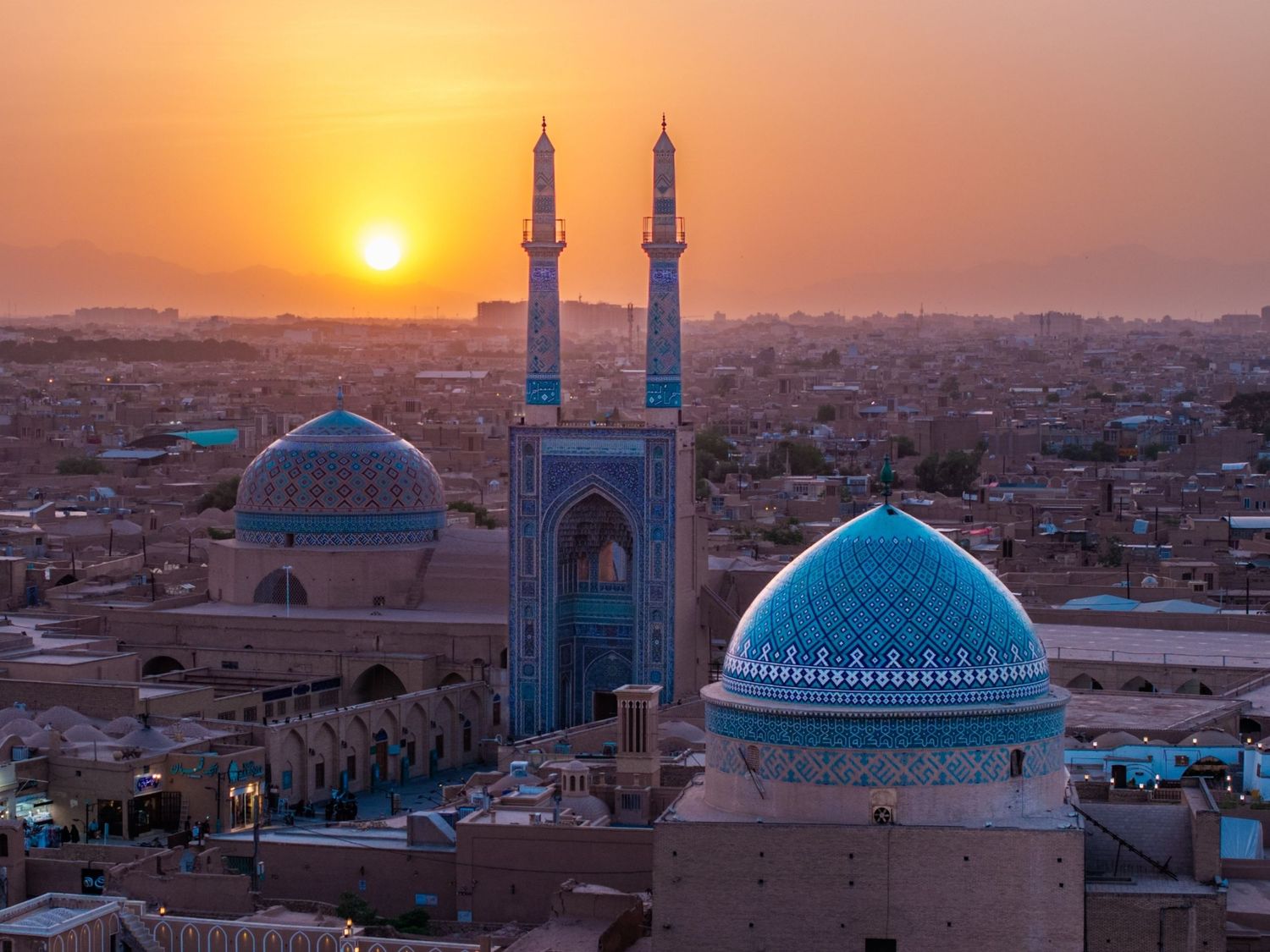 Sunset view of the Jameh Mosque's blue-tiled dome and minarets overlooking Yazd, a UNESCO World Heritage desert city in Iran.