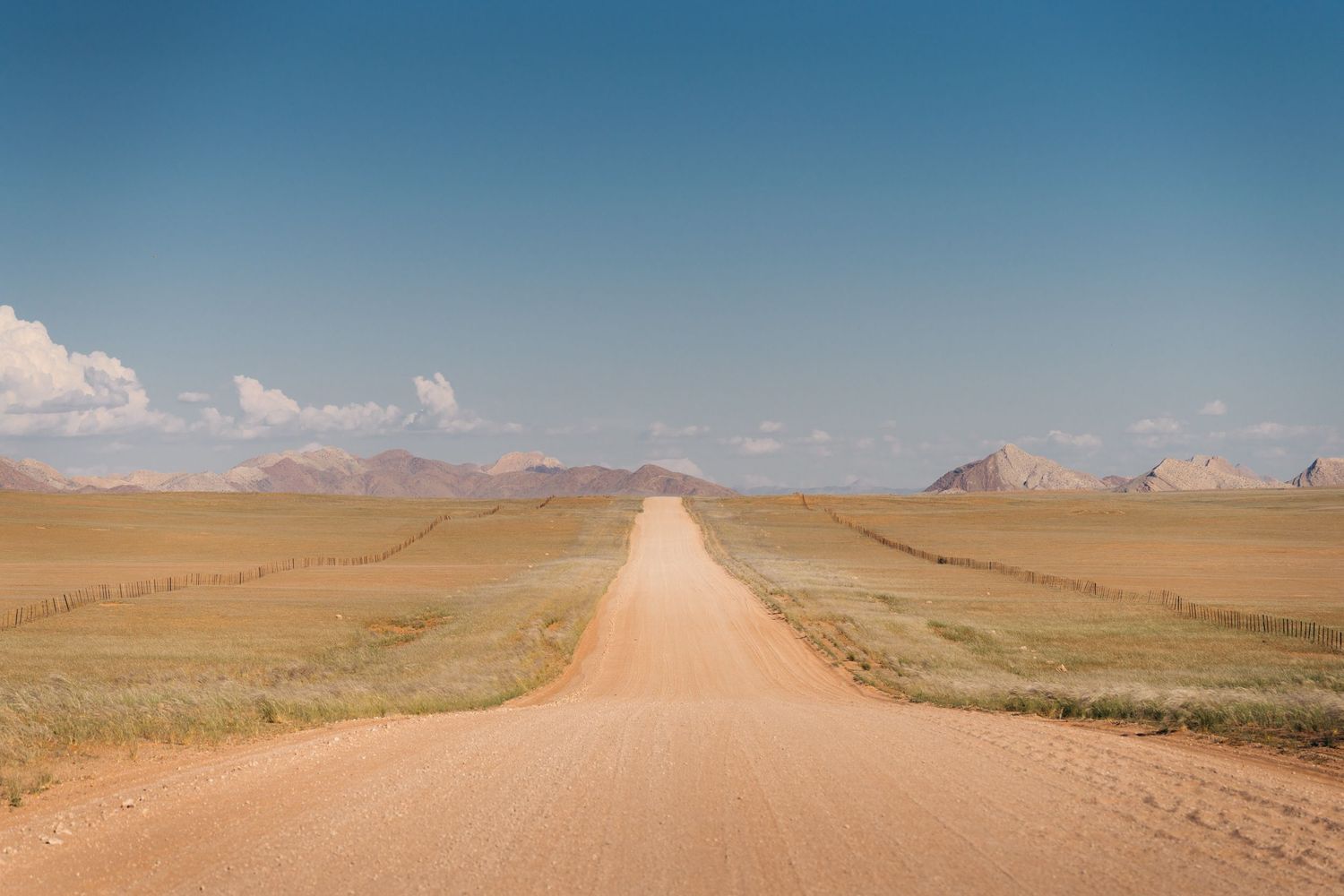 longue piste de gravier au milieu de vaste étendue de brousse avec des montagnes en arrièe-plan en namibie
