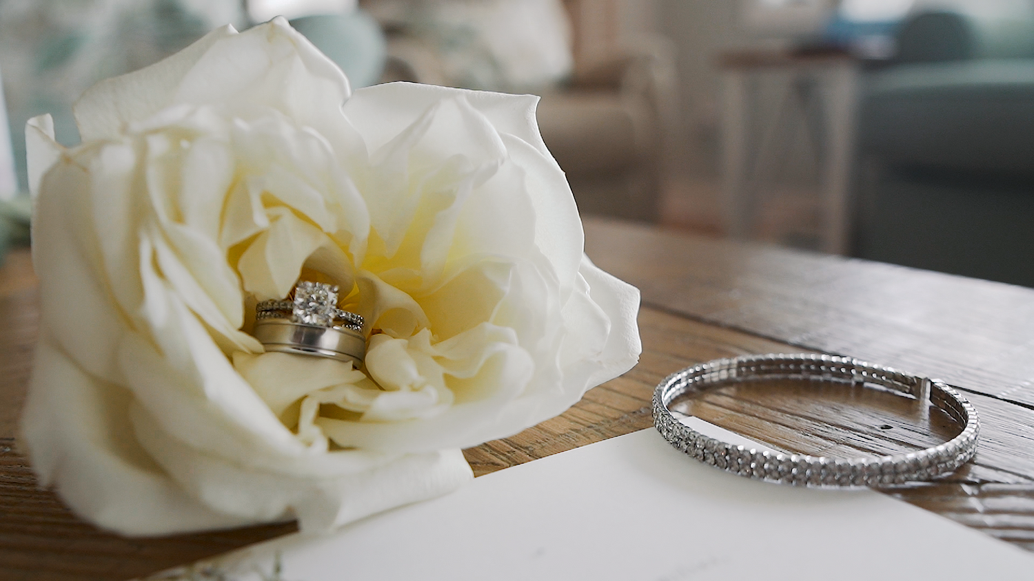 A close-up shot of a wedding ring sitting in a large white peony flower and silver bangle bracelet in a wedding video