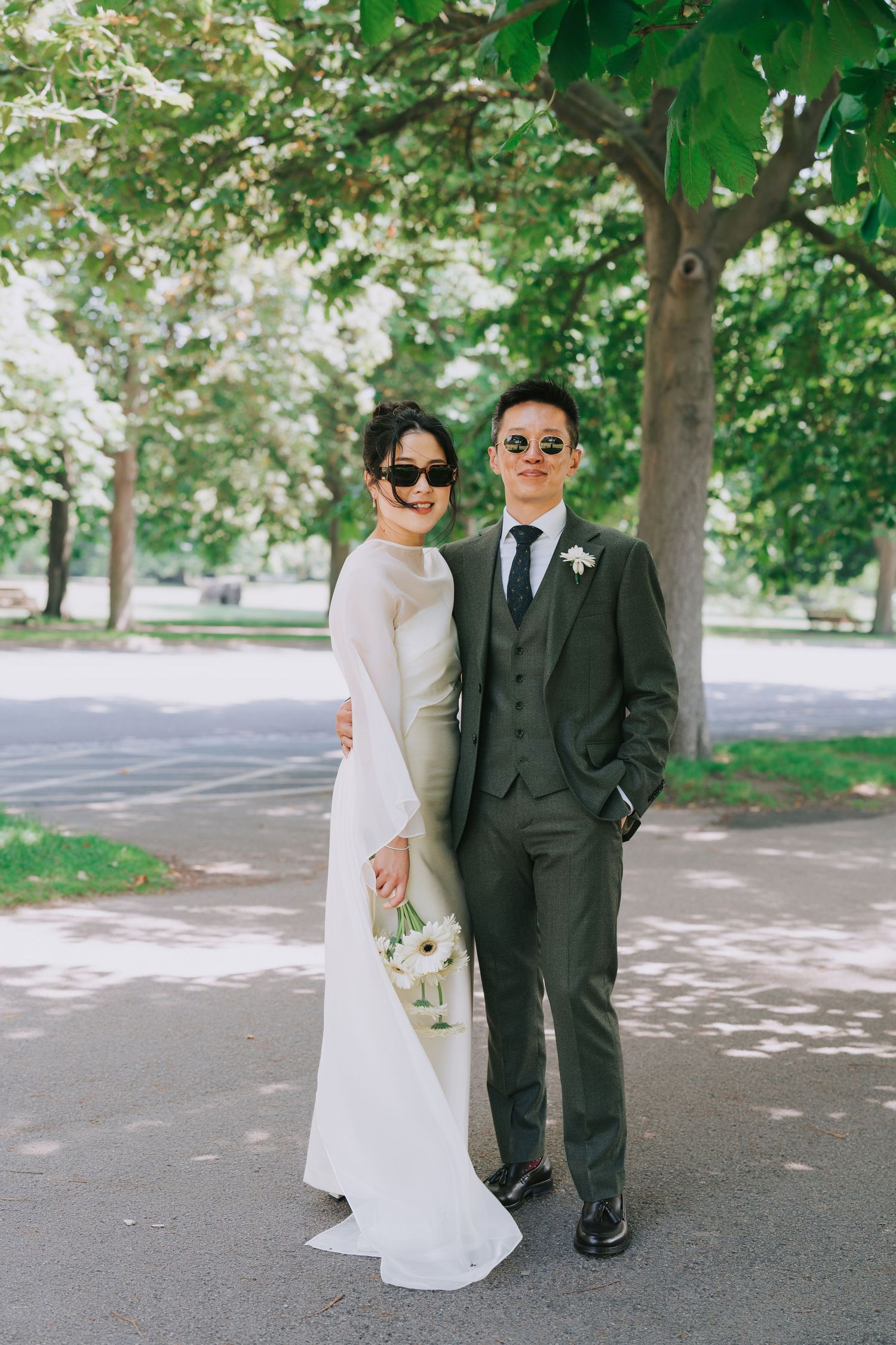 Bride in white and groom in dark suit pose together in sunglasses at at Greenwich Park London