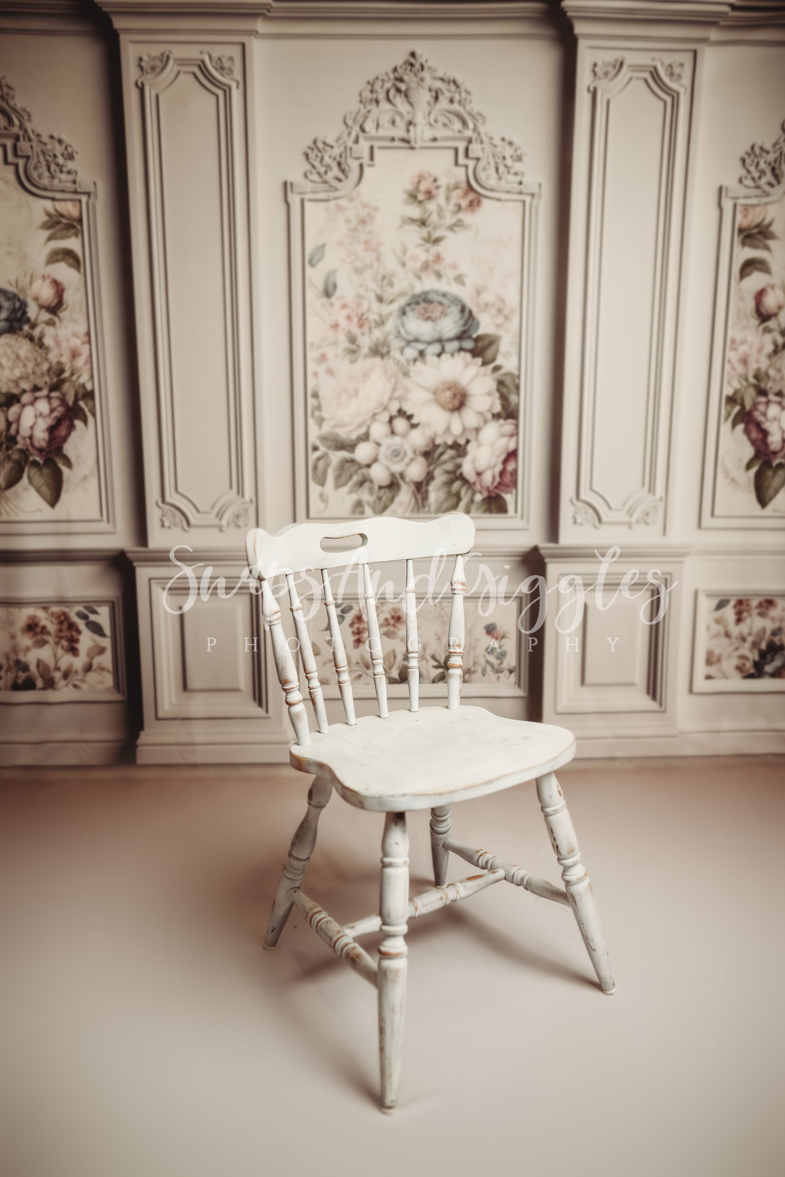Vintage white wooden chair in front of an ornate floral wall panel in a soft, romantic interior setting.