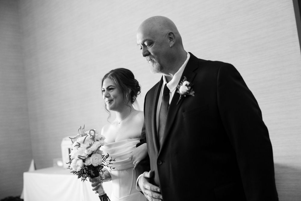 Black and white photo of a bride holding a bouquet walking with her father on her wedding day.