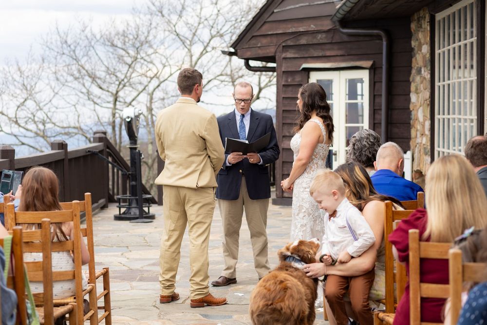 Outdoor wedding ceremony on stone patio with officiant reading vows to couple near rustic wooden lodge.