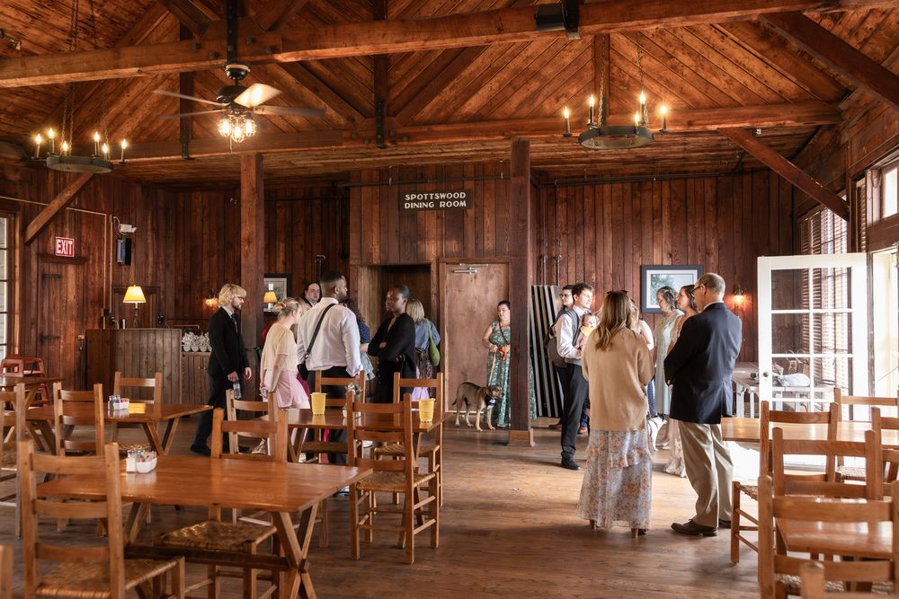 Guests mingle inside a rustic wood-paneled wedding reception venue with warm lighting and wooden furniture.