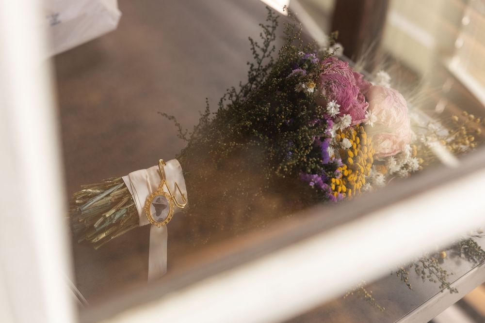 Colorful dried wildflower wedding bouquet with purple, pink and yellow blooms on wooden surface.