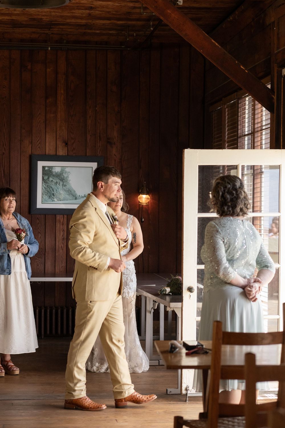 Bride and groom share first dance in rustic wood-paneled barn wedding venue with guests watching.