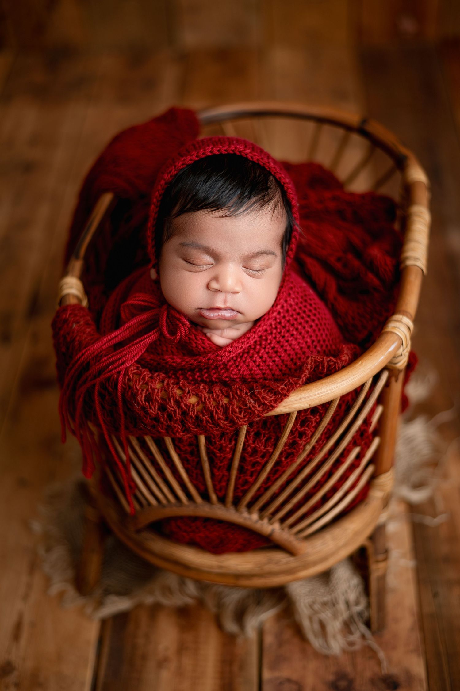 Newborn baby girl swaddled in pink knit wrap with floral headband, sleeping peacefully in rustic wooden crate.