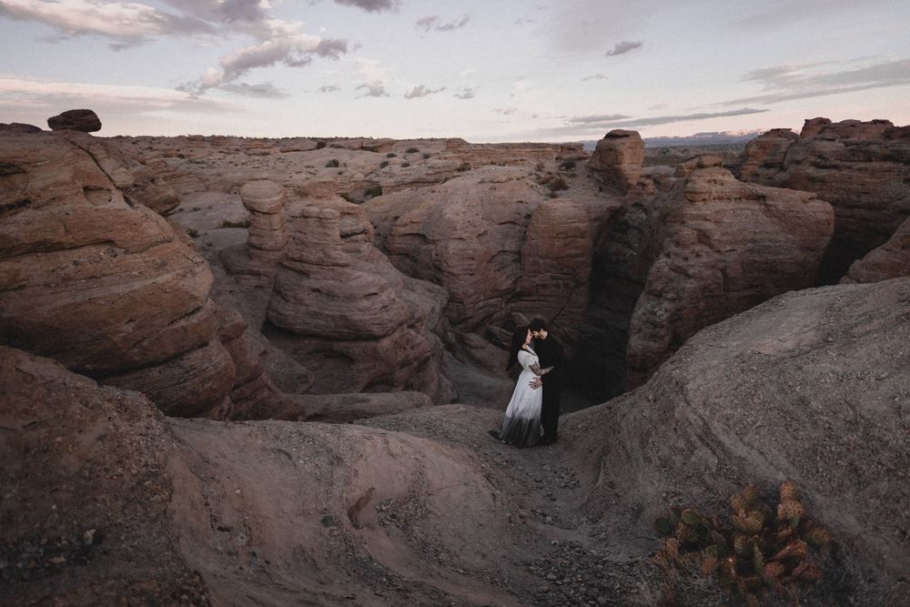 Couple embraces in a white wedding dress and black suit among towering red rock canyon formations at dusk in San Lorenzo Canyon