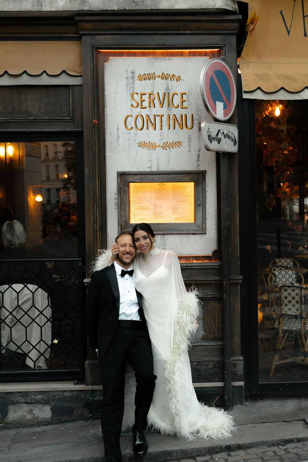 Elegant bride and groom posing in wedding attire outside a Parisian cafe with Service Continu sign.