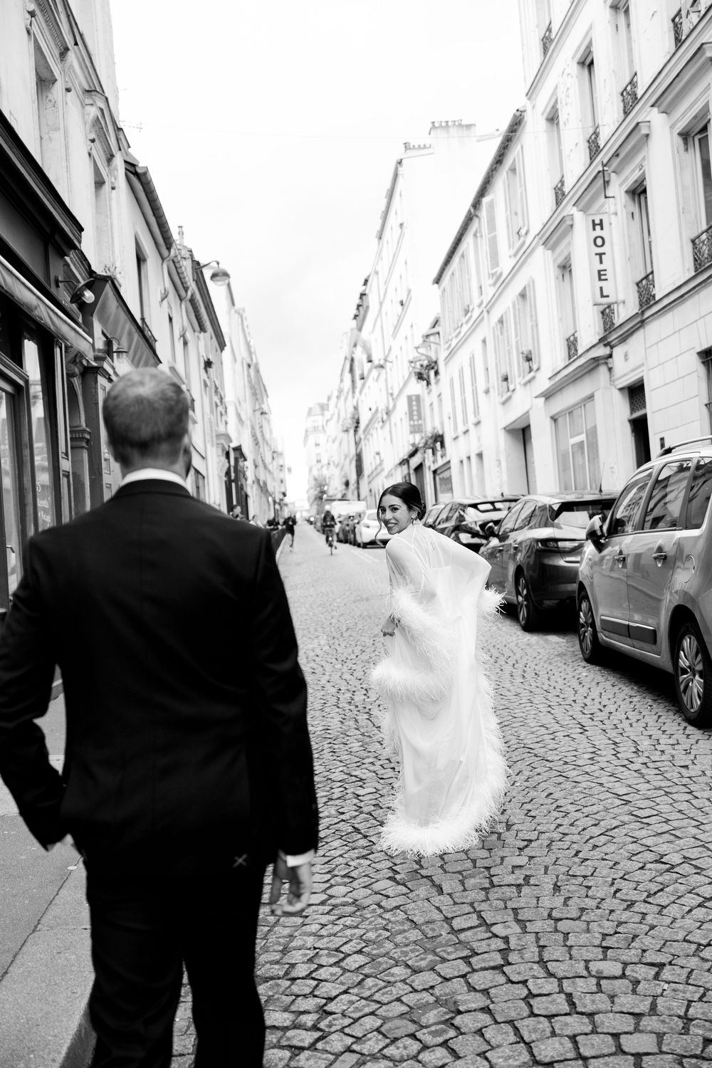 Black and white photo of a bride and groom walking on a cobblestone street in Paris, France.