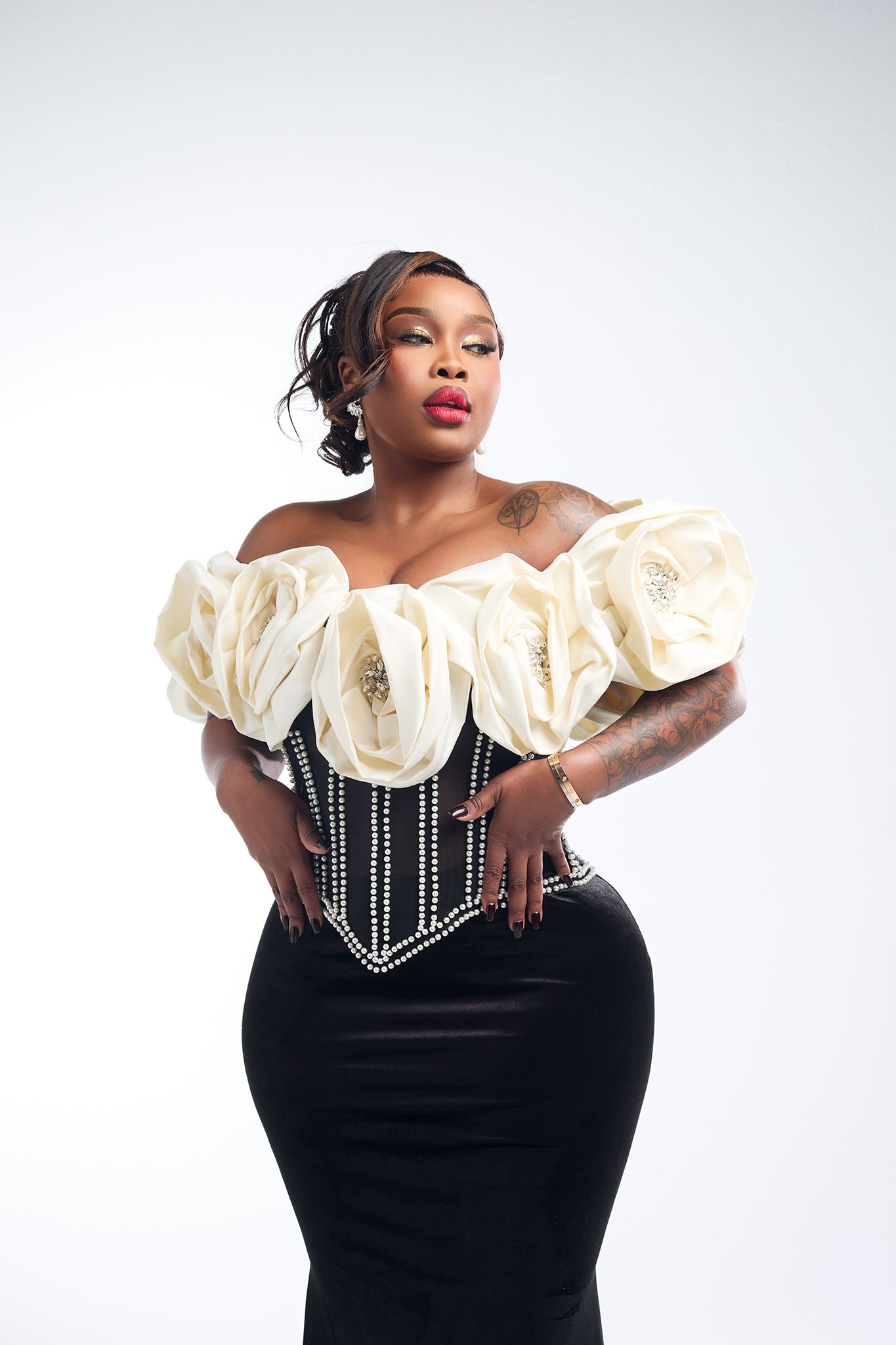 Woman in black skirt and ivory floral off-shoulder pearl corset posing in studio.