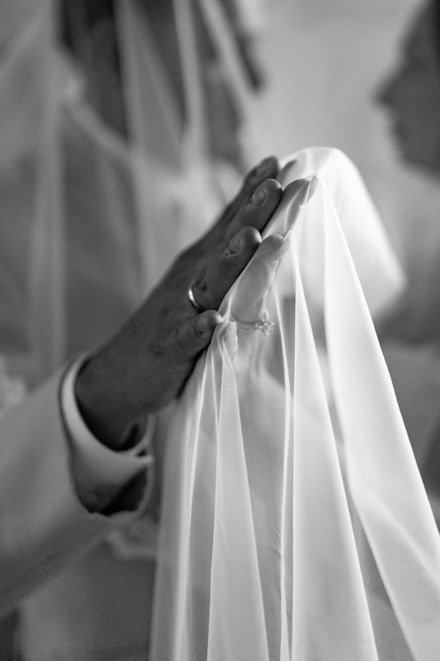 Black and white photo of bride and groom embracing at outdoor wedding altar with vineyard backdrop.