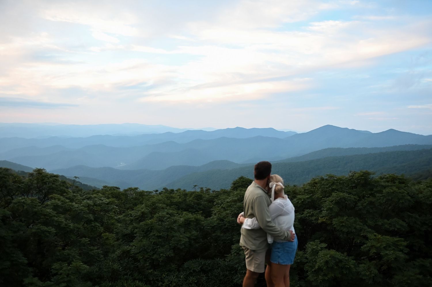 Couple embracing while overlooking stunning Blue Ridge Mountain landscape from scenic overlook at sunset.