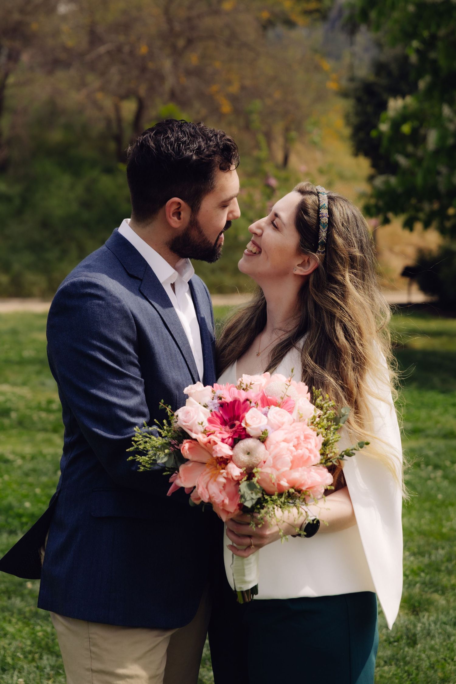 Happy couple sharing a romantic moment in a park, woman holding a pink peony bouquet.