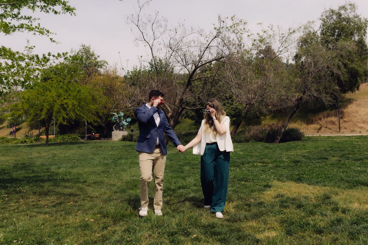 Happy couple dancing and holding hands on a green lawn surrounded by trees.