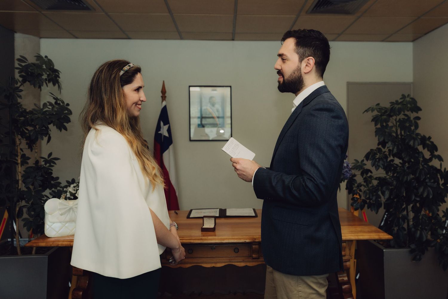 Couple exchanging vows in a cozy office ceremony with an American flag in the background.