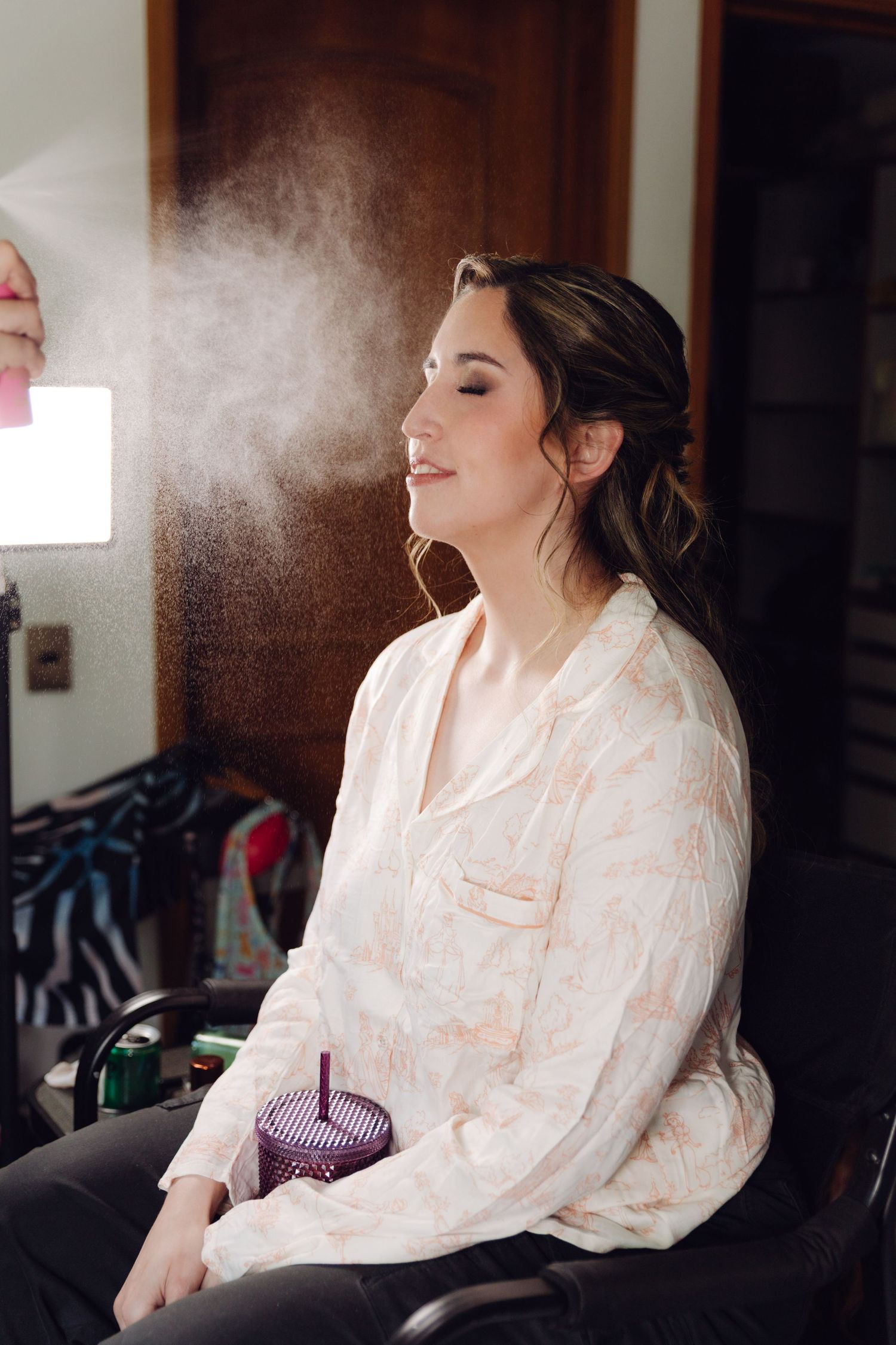 Bride smiling with eyes closed as setting spray is misted on her face.