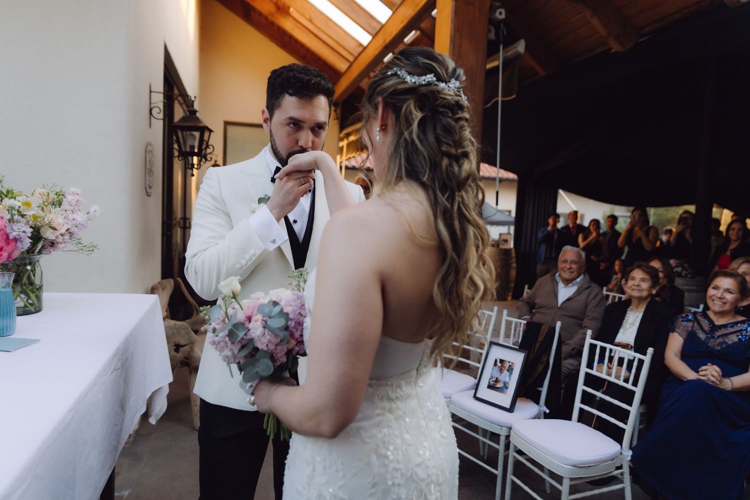 Groom kissing bride's hand tenderly during intimate wedding ceremony exchange.